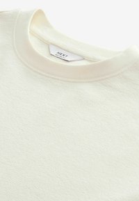 Felpa in cotone testurizzato color bianco sporco con scollatura tonda. Presenta un delicato motivo superficiale e un'etichetta con la dicitura "NEXT RELAXED FIT."
