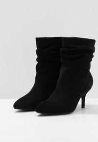 Bottes basses en daim noir avec un design décontracté, bout pointu et talon aiguille fin. Texture lisse et style minimaliste.