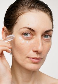 En klar hudvårdscreme appliceras på kinden med en transparent applikator. Huden verkar slät med en naturlig finish.