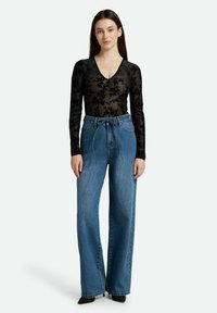 Schwarzes blumiges Spitzen-Bodysuit mit langen Ärmeln, kombiniert mit hochtaillierten, weit geschnittenen blauen Jeans, die einen gebundenen Taillenbund und subtile fransige Säume aufweisen.