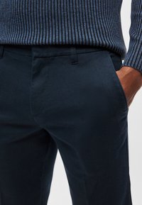 Navyblå skräddarsydda byxor med mjuk textur, utrustade med sidfickor och en klassisk passform, kombinerade med en ribbad marinblå tröja.