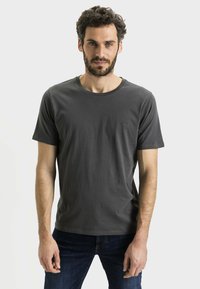 Czarny bawełniany t-shirt w kolorze ciemnoszarym, z okrągłym dekoltem i krótkimi rękawami. Ma małe, dyskretne logo na lewej piersi. Prosty design, miękka tekstura.