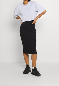 Grå kortärmad t-shirt, i croppad modell, kombinerad med en svart ribbad midi-kjol. Svarta sneakers med vita detaljer fulländar looken.