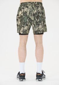 Groene en beige camouflage shorts met een elastische tailleband, gecombineerd met een zwarte binnenvoering en zwarte sportschoenen met witte sokken.