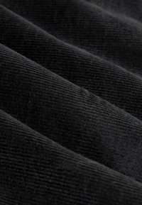 Black corduroy fabric displaying a ribbed texture, with overlapping folds emphasizing the material's soft quality and depth.