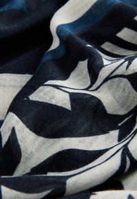 Materialul fluid prezintă un model de frunze în nuanțe de navy închis și alb. Textura este ușoară și aerisită, având un aspect ușor transparent.