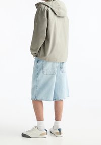 Veste à capuche gris clair, shorts en denim bleu clair et baskets blanches avec des accents bleus et beiges. Montre une coupe décontractée et un style casual.