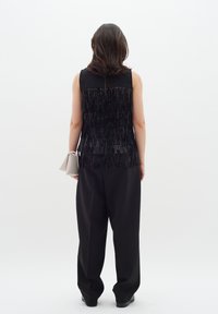 Musthave must kätisedeta tipp, millel on frantsiisidetailing, koos mustade laienevate pükstega. Heledat halli kotti hoitakse paremas käes.