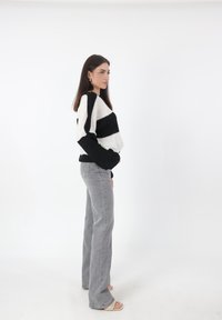 Maglione oversize a righe bianche e nere con maniche lunghe, abbinato a jeans grigi svasati e sandali aperti. Sfondo neutro.