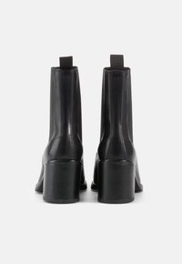 Mustad nahast pahkluu saapad läikiva viimistlusega, ristküliku kujulise kontsaga ja elastsete külgpanelitega mugavaks selga panemiseks. Sile tekstuur ja minimalistlik disain.