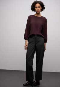 Bordowa bluzka z długim rękawem i marszczonymi mankietami, zestawiona z szarymi spodniami o wysokim stanie. Gładka tekstura, luźny krój i szyty na miarę design.