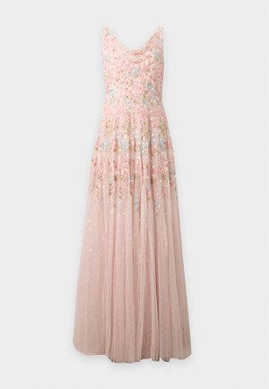 Femme aux longs cheveux foncés portant une robe maxi rose clair sans manches brodée de fleurs, debout devant un fond blanc uni.