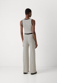 Czarny i biały striped kombinezon z dopasowanym góry i szerokimi nogawkami. Wykonany z miękkiego materiału, ma ściągniętą talię i brak widocznych zapięć.