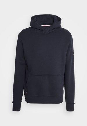 Felpa con cappuccio blu navy scuro con maniche lunghe, tasca a marsupio frontale e toppa sul braccio superiore sinistro, mostrata su uno sfondo semplice.