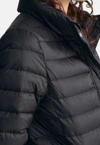Black puffer jacket with a high collar, featuring quilted sections and small hardware accents. Material appears smooth and lightweight.