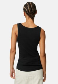 Svart ärmlös tanktopp i ribbat tyg, med rund halsringning och figursydd silhuett. Bakstycket är slätt med en lätt böjd nederkant.