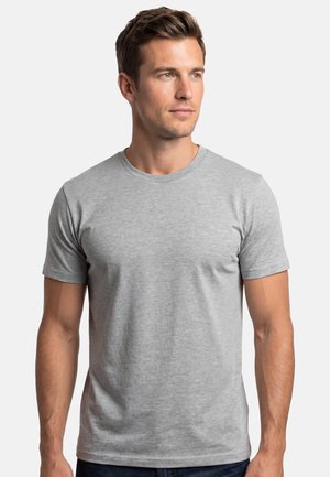 Mand med kort brunt hår iført en ensfarvet, lysegrå T-shirt med rund hals og korte ærmer, der kigger let til højre, på hvid baggrund.