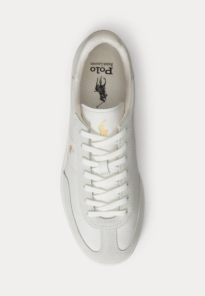 Fehér bőr sportcipő fűzővel, arany Polo Ralph Lauren logóval a nyelvén és oldalán, párnázott talpbetéttel, amelyen Polo Ralph Lauren márkajelzés található.
