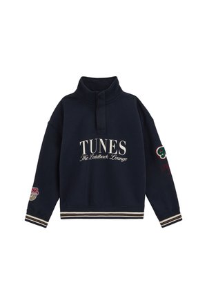 Granatowy sweter z wysokim kołnierzem, tekstem z przodu "TUNES The Laidback Lounge,", paski na mankietach i dole, oraz haftowanymi naszywkami na rękawach.