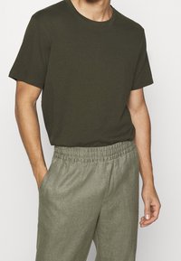 Tummanvihreä puuvillapaita, jossa on lyhyet hihat ja pyöreä pääntie, yhdistettynä vaaleanharmaisiin joustaviin housuihin. Sileä tekstuuri.