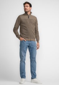 Suéter cremallo con cremallera y un patrón de punto texturizado, combinado con jeans azul claro y zapatillas blancas. Diseño ajustado con cuello alto.
