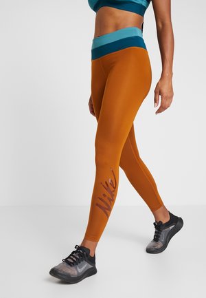 Legginsy Nike w kolorze pomarańczowym o gładkiej fakturze; mają turkusowy pas i logo na lewej nogawce. W połączeniu z czarnymi butami sportowymi.