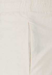 Tissu beige clair avec une texture lisse, doté d'une taille élastique et d'une couture latérale pour plus de confort et de facilité.