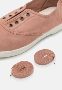 Różowy płócienny sneaker z fakturowanym wykończeniem, z okrągłymi metalowymi oczkami, białą gumową podeszwą i dwoma dopasowanymi sznurówkami zwiniętymi obok.