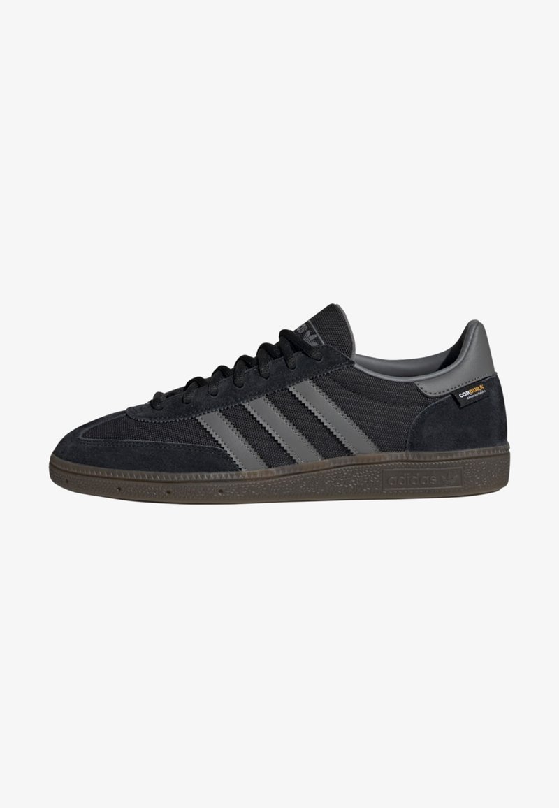 Schwarze Wildledersneaker mit grauen Netzpaneelen, ausgestattet mit drei grauen Streifen, einer Gummisohle und einem kleinen Logo an der Ferse.