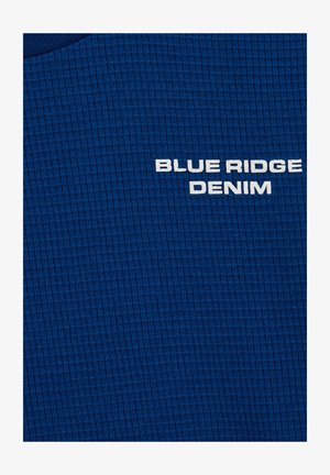 Zila teksturēta auduma ar režģa rakstu tumši zila krāsā, uz kura ir teksts "BLUE RIDGE DENIM" baltā krāsā.