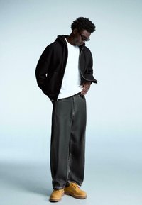 Černá mikina na zip, bílý tričko, voln�é šedé kalhoty, béžové robustní boty. Obsahuje texturovanou tkaninu a volný střih pro pohodlí.