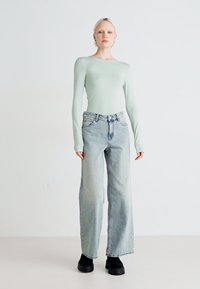Lys grønn langermet topp kombinert med høylivede lyseblå vide jeans og svarte platåsko; glatt tekstur med minimal detaljer.