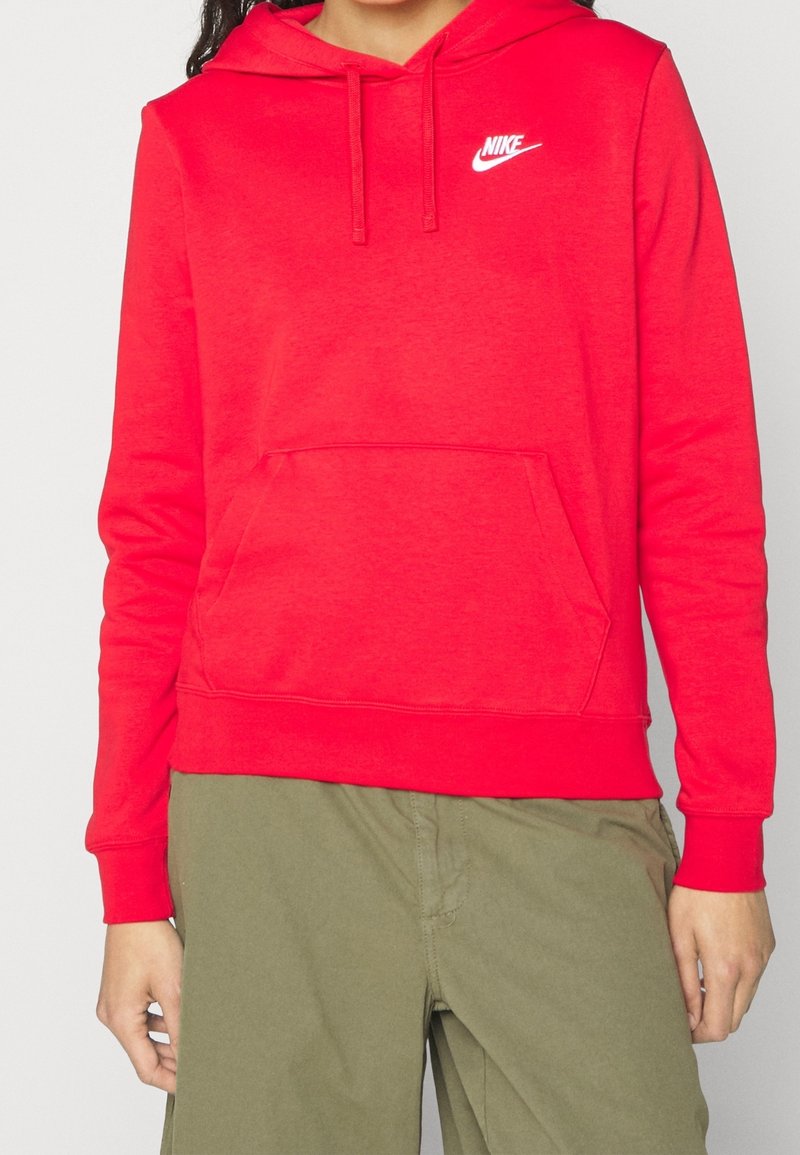 Sweat à capuche en coton rouge avec une poche avant, une capuche à cordon et le logo Nike blanc sur le côté gauche de la poitrine. Associé à un pantalon vert olive.