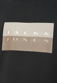 Μαύρο μπλουζάκι με υφασμένο ορθογώνιο σχέδιο που φέρει τα λόγια "JACK & JONES" σε ανάγλυφα μπεζ γράμματα.