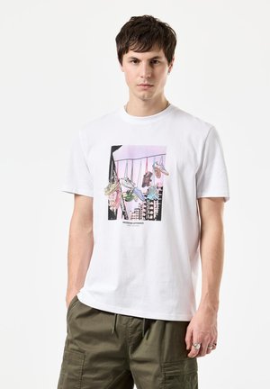 White cotton t-shirt featuring a graphic print of hanging sneakers in various colors, with a black outline and pastel background.