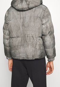 Grå puffjacka med huva, med en texturerad design och sydda paneler. Elastiska ärmslut och nederkant ger en tät passform.