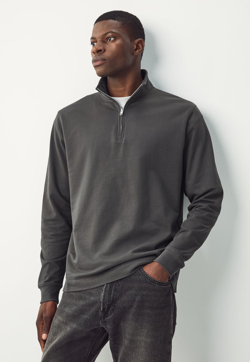 Felpa con cappuccio grigio scuro con collo a mezza zip, maniche lunghe, texture morbida e vestibilità comoda, abbinata a jeans scuri.