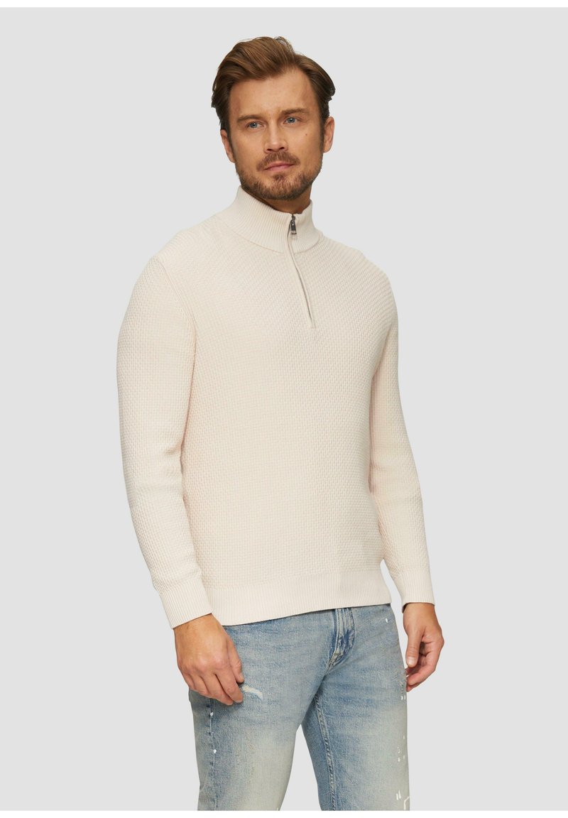 Pull léger beige à col haut, avec un motif de tricot texturé et une fermeture éclair à l'avant. Assorti à un jean déchiré bleu clair.