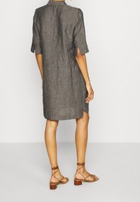 Šedé lněné šatové šaty s ohrnutými krátkými rukávy a bočními rozparky, doplněné o světlé hnědé sandály na pásky na jednobarevném neutrálním pozadí.