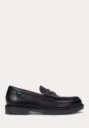 Mocassin en cuir noir avec semelle robuste et étiquette Polo verte sur le côté, présentant des détails cousus et un design sans lacets.