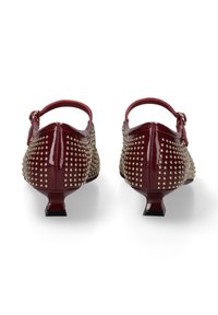 Chaussures en cuir verni bordeaux avec clous dorés, design à bride arrière, petits talons blocs et accents texturés, présentant une petite sangle avec boucle.