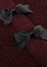 Två svarta grosgrain-ribbonbågar på strukturerad mörk burgunderryarn, som framhäver kontrasten mellan de släta bågarna och den fluffiga tröjmaterielen.