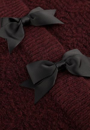 Twee zwarte grosgrain lintstrikken op een textuur van donker bordeauxrood breiwerk, die het contrast benadrukken tussen de gladde strikken en het fuzzy sweatermateriaal.
