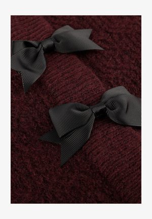 Twee zwarte grosgrain lintstrikken op een textuur van donker bordeauxrood breiwerk, die het contrast benadrukken tussen de gladde strikken en het fuzzy sweatermateriaal.