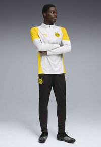 Ropa deportiva Puma que incluye una camiseta de manga larga gris y amarilla con cuello con cremallera y pantalones negros con un logo, diseñada para uso atlético.