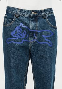 Σκούρα μπλε τζιν denim με μεγάλο μοβ σκίτσο σκύλου στο μπροστινό μέρος του άνω μηρού.