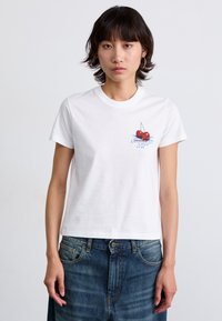 Camiseta de algodón blanca con cuello redondo, que presenta un pequeño gráfico de cerezas rojas y letras azules en el lado izquierdo del pecho.