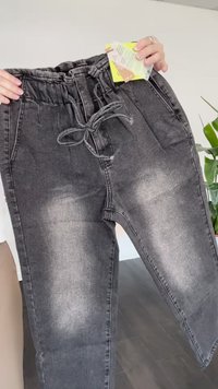 Fekete farmernadrág rugalmas derékkal és állítható zsinórral. A combokon világosabb fakulási minták figyelhetők meg. Gondozási címkék is találhatók benne.
