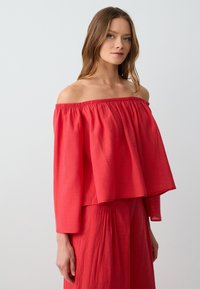 Rotes, schulterfreies Oberteil mit weitem Schnitt und langen Ärmeln. Hergestellt aus leichtem Stoff mit gerafftem Ausschnitt und Bund.