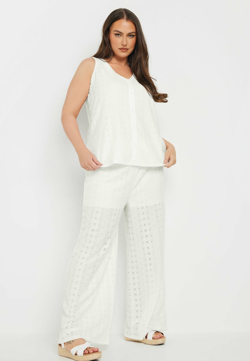 Set composto da top bianco senza maniche e pantaloni a gamba larga, con motivo floreale a intagli e tessuto strutturato; abbinato a sandali espadrilles bianchi.